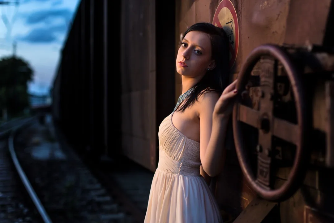 Portrait of a woman in a white dress beside an old train carriage by Andreas Düren